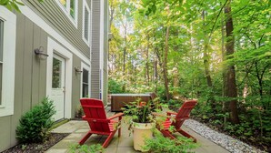 Eine Terrasse mit zwei roten Adirondack-Stühlen, einer Holztonne als Whirlpool und einem Blumentopf.