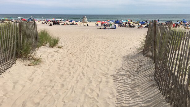 Ein Sandstrand mit einer Holzlattenzaun, Sonnenschirmen und Personen.