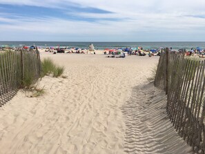 Ein Sandstrand mit einer Holzlattenzaun, Sonnenschirmen und Personen.