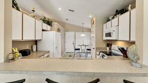 A modern kitchen with white cabinets, a central island, and a dining area with a table and chairs. - Minutes from Disney - Beautiful 3/2 Pool Villa with WiFi in Hampton Lakes  (Davenport)