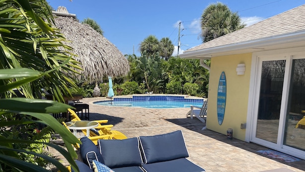 A poolside area with lounge chairs, a thatched roof structure, and a pool.