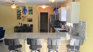 A kitchen with a central island, bar stools, a refrigerator, and a microwave.
