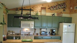 Una cocina con armarios verdes, un microondas blanco, una estufa, un tostador y un refrigerador.