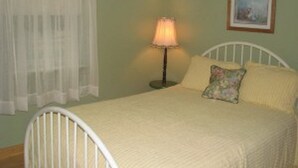 Una cama con estructura metálica blanca, una lámpara de noche y un cojín estampado con flores.