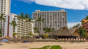 A beachfront hotel with multiple high-rise buildings, palm trees, and a thatched-roof structure.