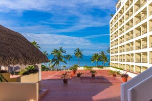 Un patio de hotel con vista al océano, palmeras y una estructura de techo de paja.