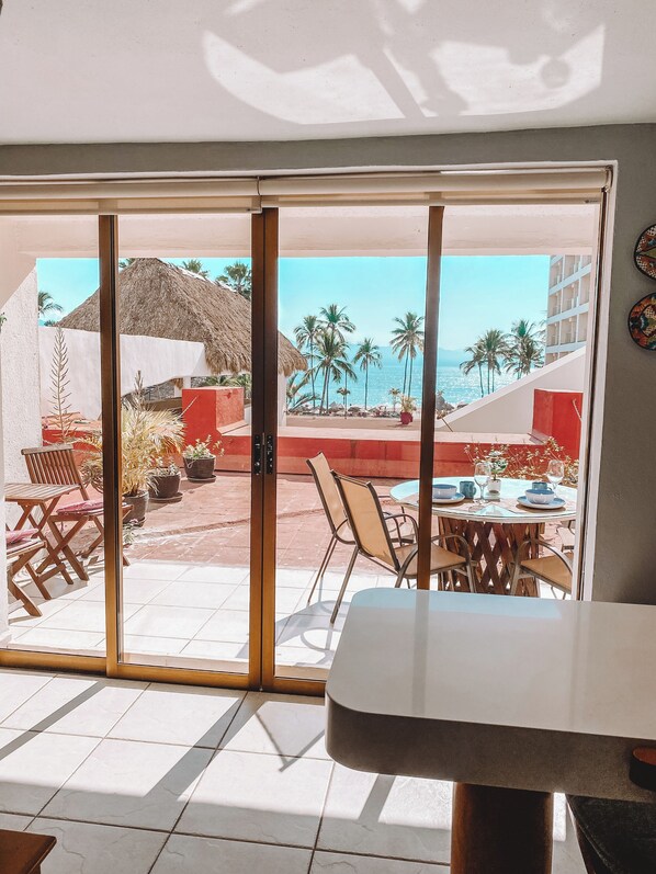 Una habitación con puerta de vidrio corrediza que da a un patio exterior con mesa lista para comer, sillas y plantas en macetas.