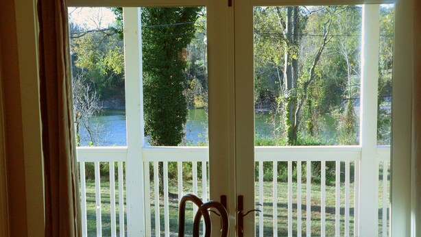 A view from a porch with a wooden railing, overlooking a lake and trees.