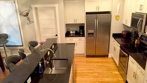 A modern kitchen with a black countertop, stainless steel appliances, and wooden flooring.