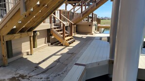 Una terraza de madera con una escalera que lleva a una zona cubierta, una piscina y vistas a un barrio residencial.
