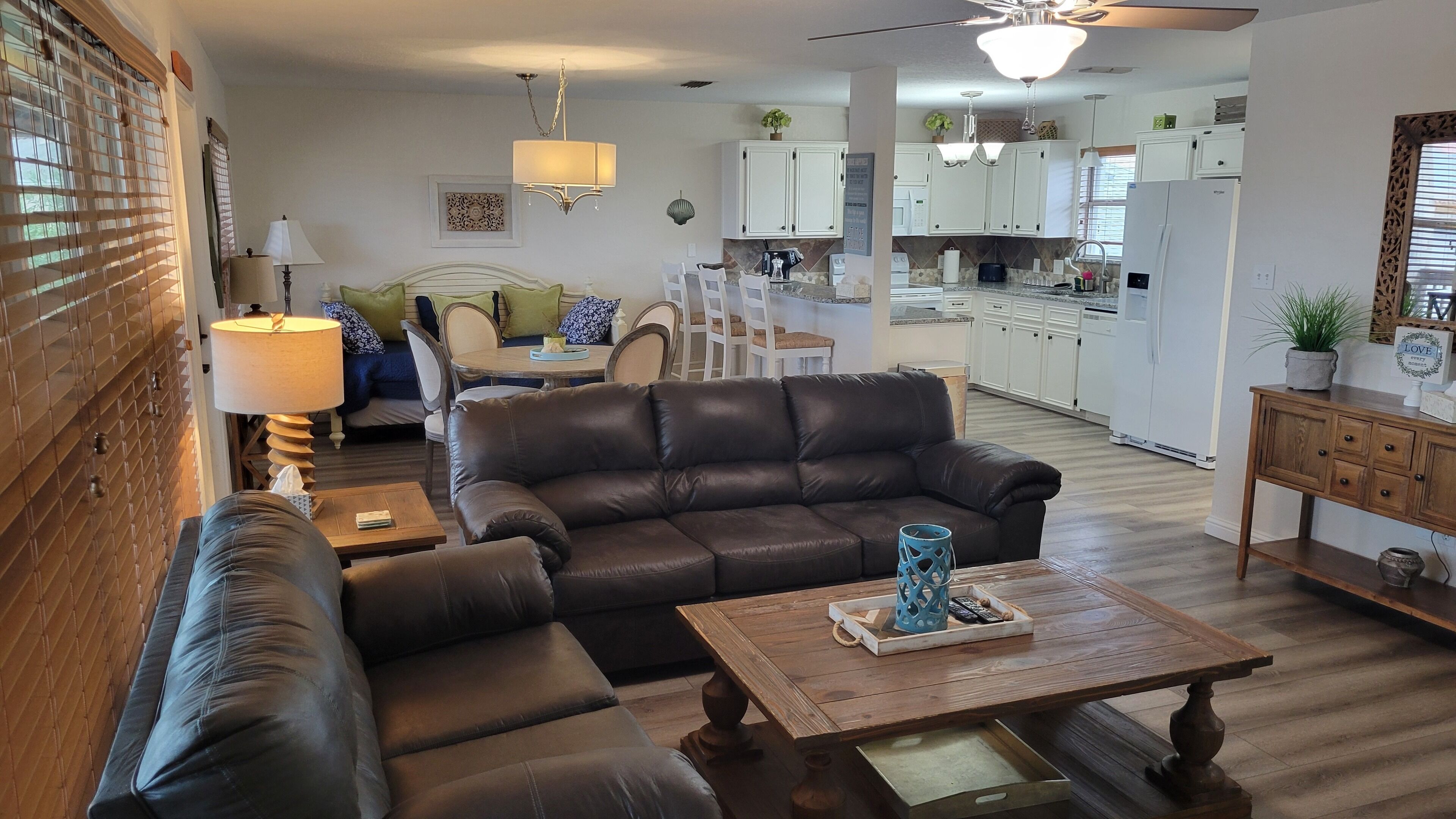 A living room with a brown leather sofa, a wooden coffee table, and a dining area with a white table and chairs.