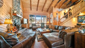 A cozy log cabin interior with a fireplace, leather sofas, and a stone wall. - Dancing Bear Lodge, Pine AZ; Luxury Cabin with Views, Spa & Outdoor living area (Pine)