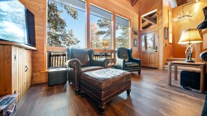A cozy log cabin interior with a large wooden bed, leather armchairs, and a dining area. - Dancing Bear Lodge, Pine AZ; Luxury Cabin with Views, Spa & Outdoor living area (Pine)