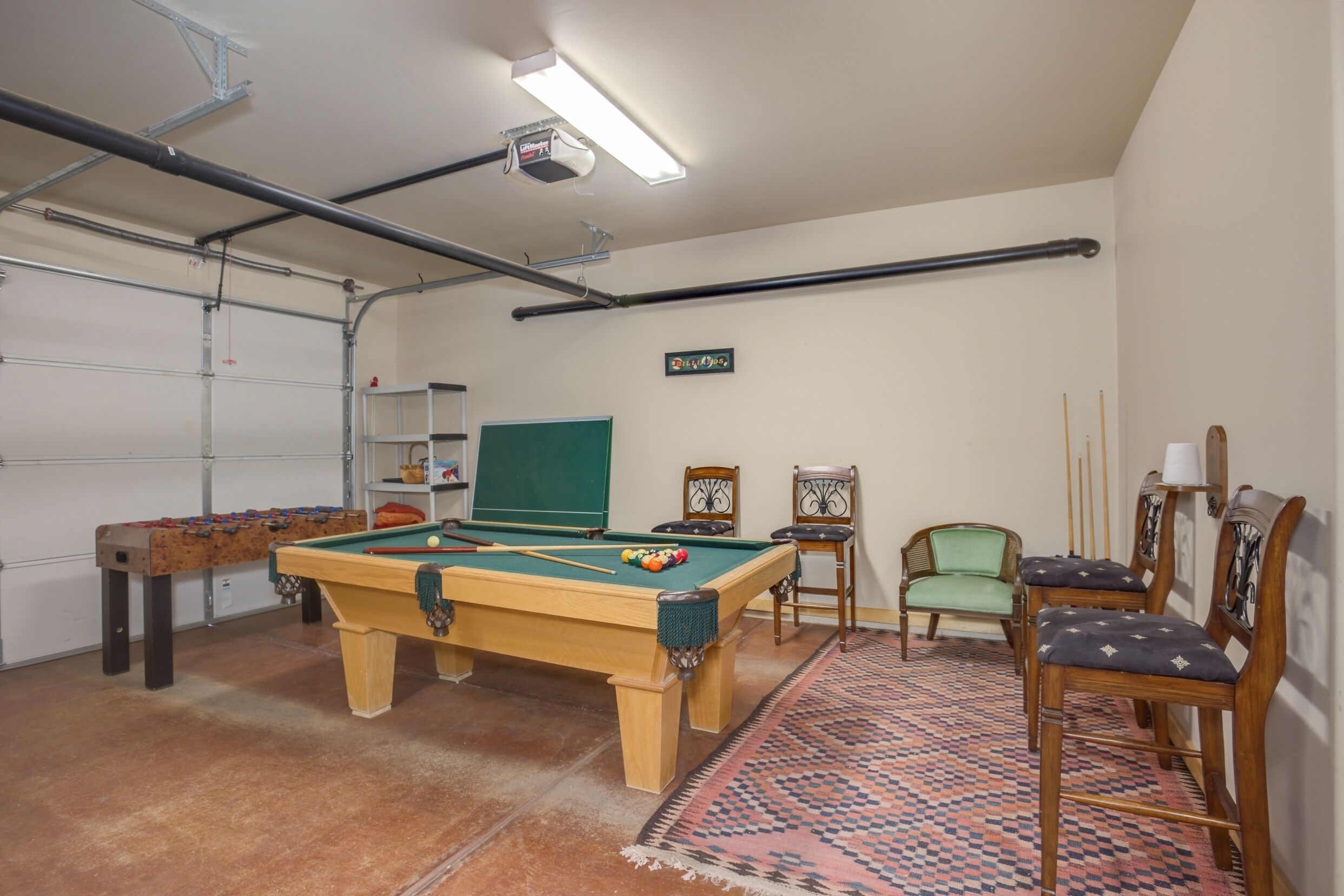 Ett biljardbord med biljardbollar, en grön tavla och ett fotbollsspel i ett rum med ett mönstrat mattgolv och trästolar.
