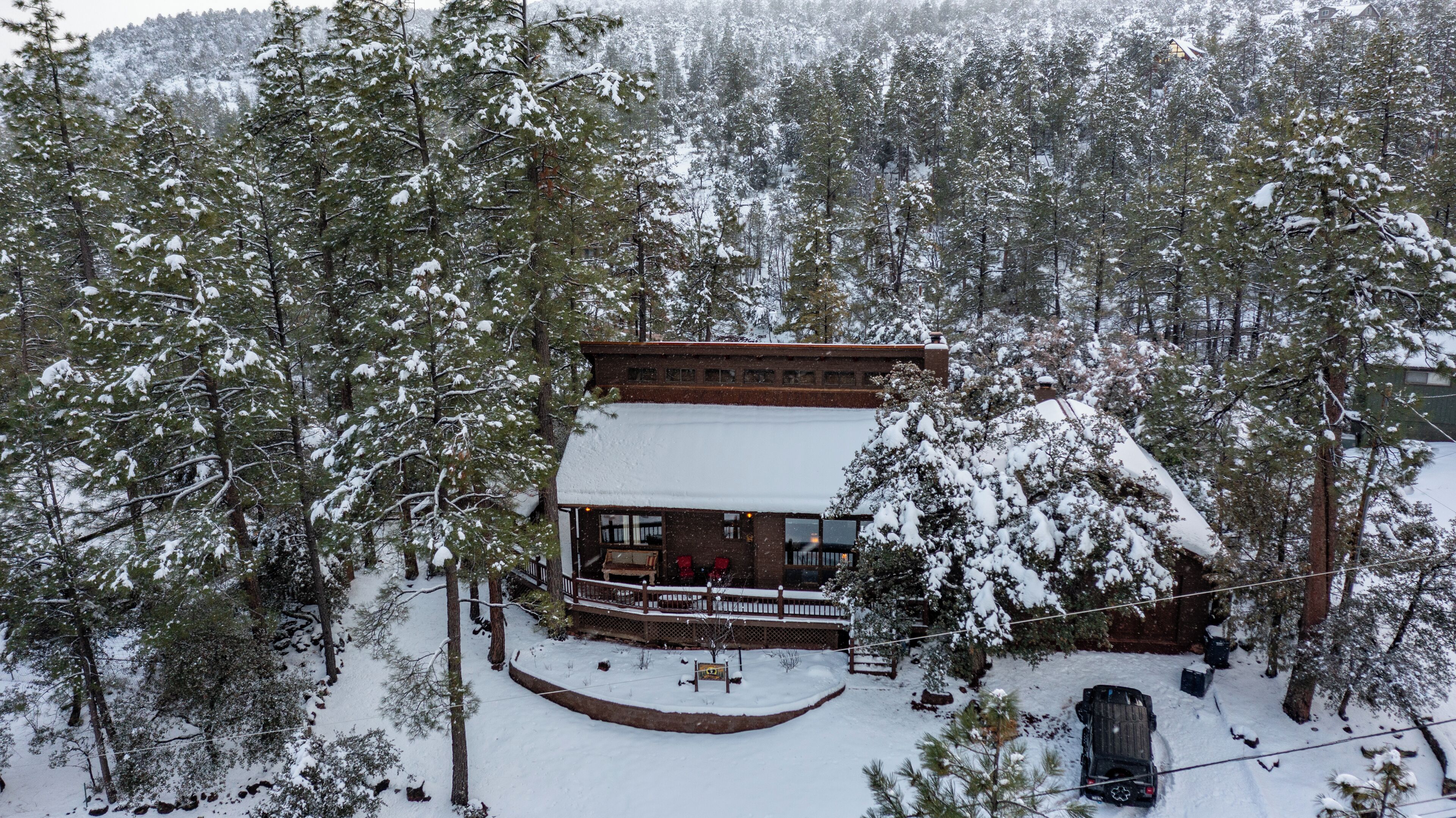 Una cabaña con porche cubierto y terraza cercada, rodeada de árboles cubiertos de nieve.