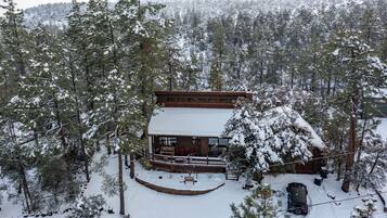 Una cabaña con porche cubierto y terraza cercada, rodeada de árboles cubiertos de nieve.