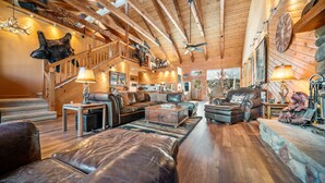 A spacious living room with leather furniture, a staircase, and a kitchen in the background. - Dancing Bear Lodge, Pine AZ; Luxury Cabin with Views, Spa & Outdoor living area (Pine)