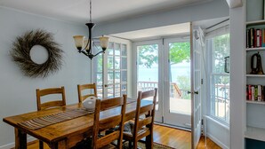 A dining area with a wooden table and chairs, a chandelier, a bookshelf, and a view of the outdoors.