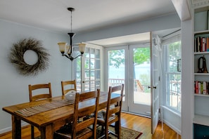 A dining area with a wooden table and chairs, a chandelier, a bookshelf, and a view of the outdoors.