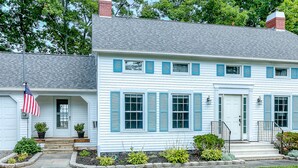 A two-story house with a front porch, a flag, and a well-maintained lawn.