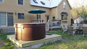 A hot tub on a wooden platform in front of a house with a deck, surrounded by outdoor furniture. - Quintessential farmhouse with hot tub, mountain views, sparkling clean (North Conway)