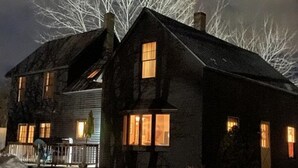 A two-story house with a porch and a snow-covered yard at night. - Quintessential farmhouse with hot tub, mountain views, sparkling clean (North Conway)
