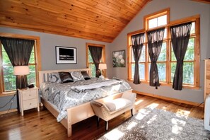 Une chambre spacieuse avec un grand lit, un plafond en bois et de nombreuses fenêtres dotées de rideaux.
