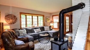 A cozy living room with a fireplace, a sofa, a coffee table, and a large window. - Quintessential farmhouse with hot tub, mountain views, sparkling clean (North Conway)
