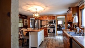 A spacious kitchen with wooden cabinets, stainless steel appliances, and a central island. - Quintessential farmhouse with hot tub, mountain views, sparkling clean (North Conway)