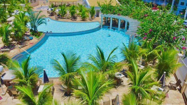Una piscina amplia y luminosa rodeada de palmeras y sillas de descanso, con vistas a edificios de hotel al fondo.