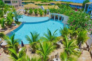Una piscina amplia y luminosa rodeada de palmeras y sillas de descanso, con vistas a edificios de hotel al fondo.