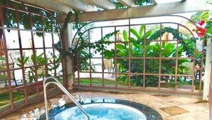 Un jacuzzi con barandilla de metal, rodeado por un patio con baldosas y abundante vegetación.