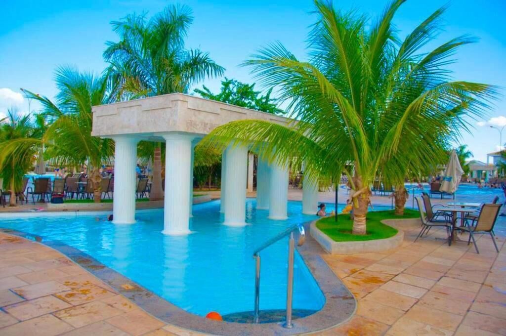 A pool area with palm trees, a covered seating area, and outdoor dining tables.