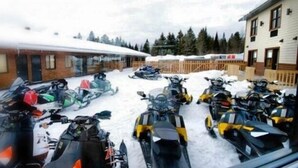 A view of a building with a snow-covered roof and a row of snowmobiles parked in front. - Hôtel Roquemont (Saint-Raymond)