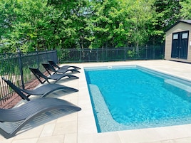 Piscina retangular com deck revestido e cerca de metal preta.