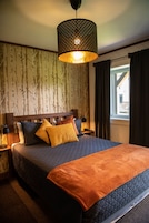 Quarto com cama grande, luminária pendente e janela com cortinas.
