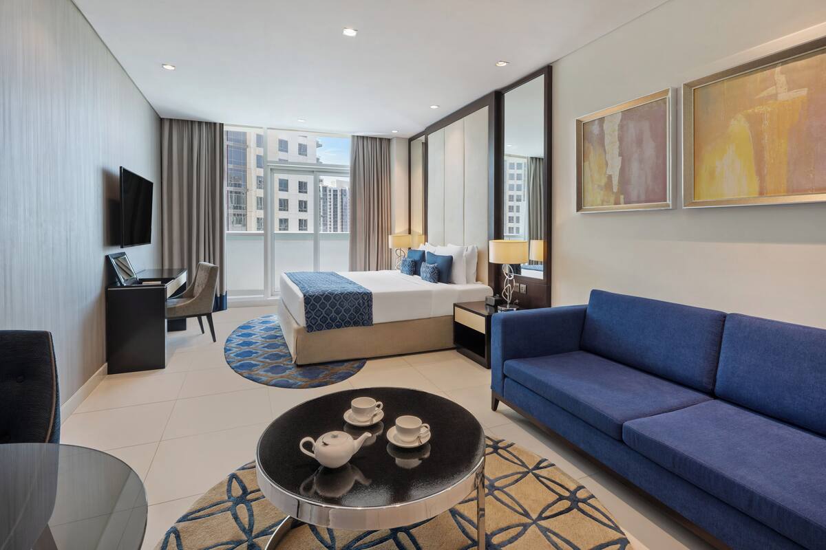 Una habitación de hotel moderna con cama, sofá, televisión, escritorio y vistas a la ciudad.