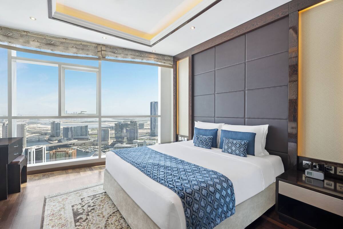 Habitación de hotel moderna con una cama grande, una mesita de noche y vistas a la ciudad.