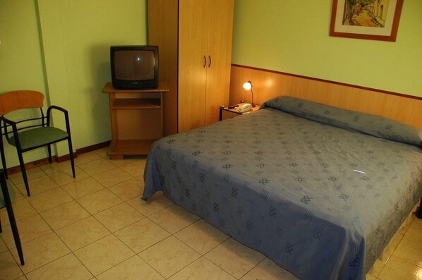 A bedroom with a bed, a chair, a television on a stand, and a nightstand with a lamp.