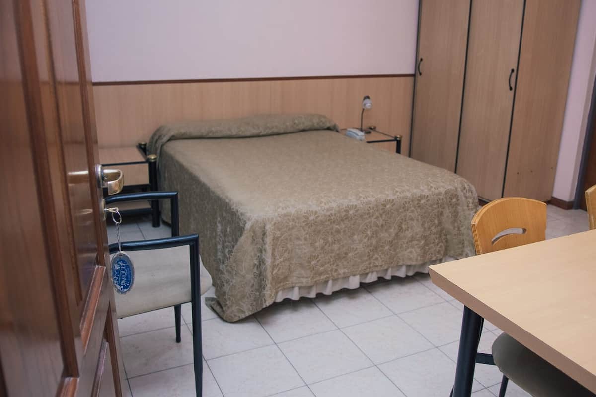 A bedroom with a bed, a desk, a chair, a wardrobe, and a door.