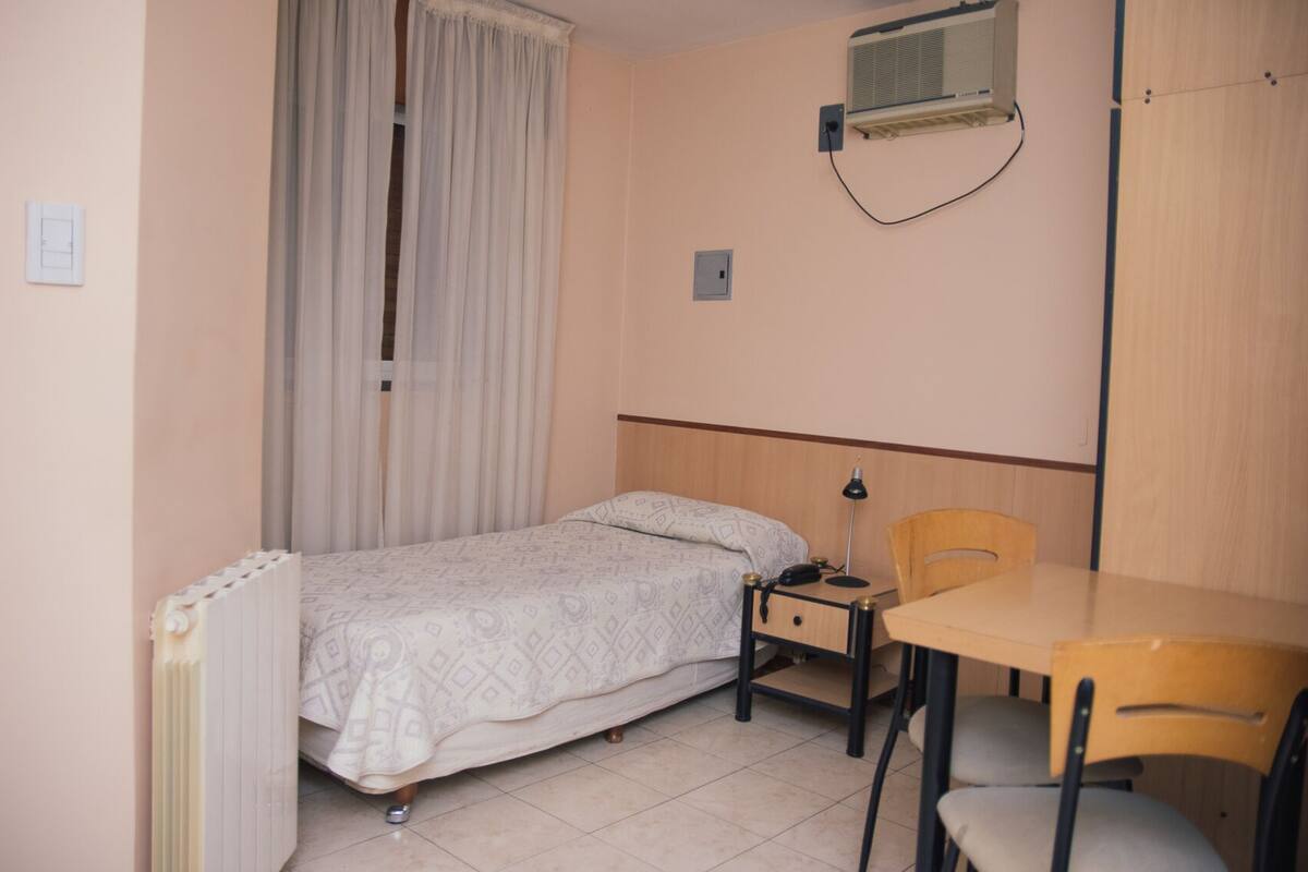 A bedroom with a bed, a desk, a chair, and a radiator.