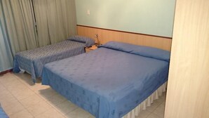 Habitación de hotel con dos camas individuales, cabecera de madera, una mesita con lámpara y una ventana con cortinas.