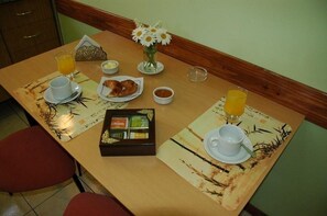A breakfast table with a vase of flowers, a tray of croissants, orange juice, and a box of tea.