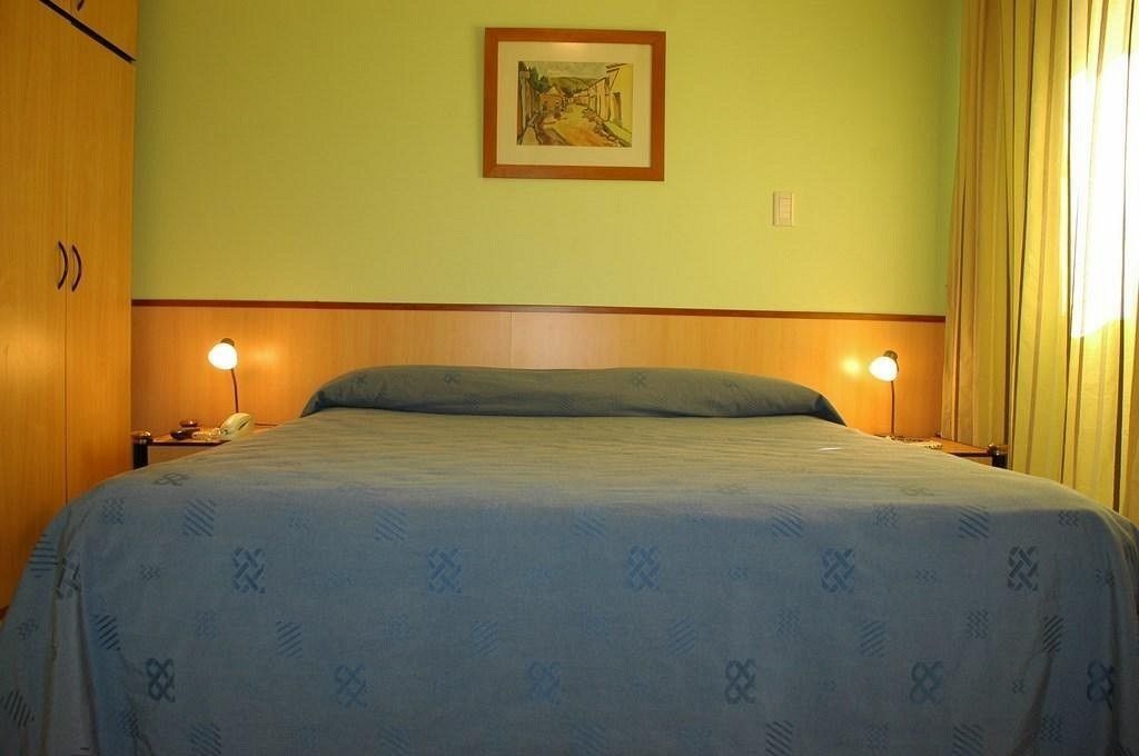 Ein Schlafzimmer mit einem Bett, zwei Nachttischlampen, einem Telefon und einem gerahmten Bild an der Wand.