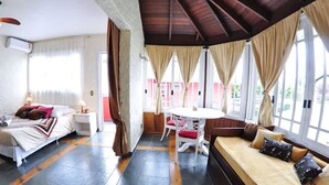 A hotel room with a bed, a sofa, a dining table with chairs, and large windows with curtains. - Aardvark Inn Pousada (Gramado)