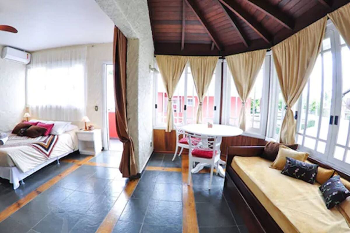 Ein Hotelzimmer mit Bett, einer Couch, einem Esstisch mit Stühlen und großen Fenstern mit Vorhängen.