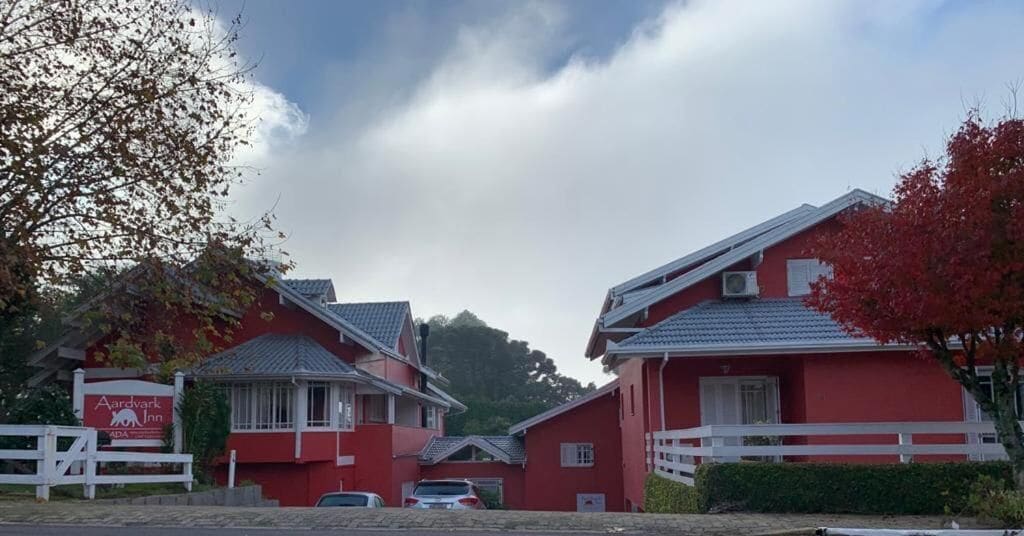 Un bâtiment rouge avec une clôture blanche, une enseigne indiquant « Aardvark Inn », et une voiture garée devant.