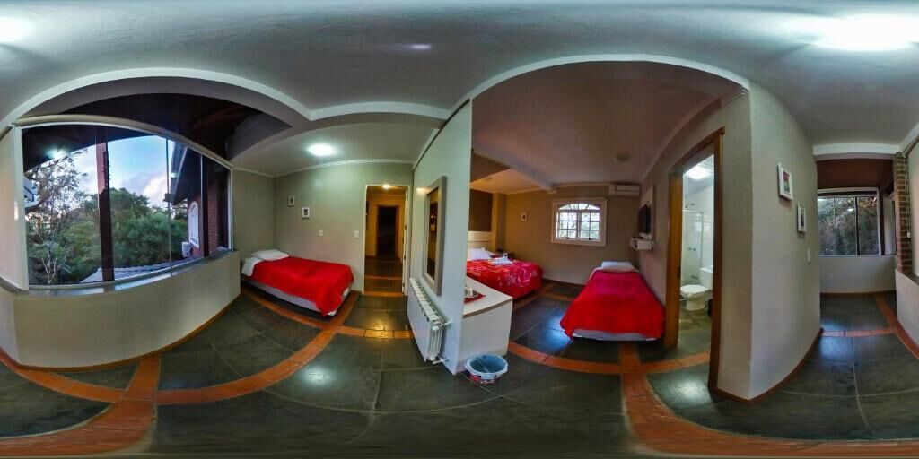 Een panoramisch uitzicht op een hotelkamer met twee bedden, een klein bureau en een raam met zicht op bomen.