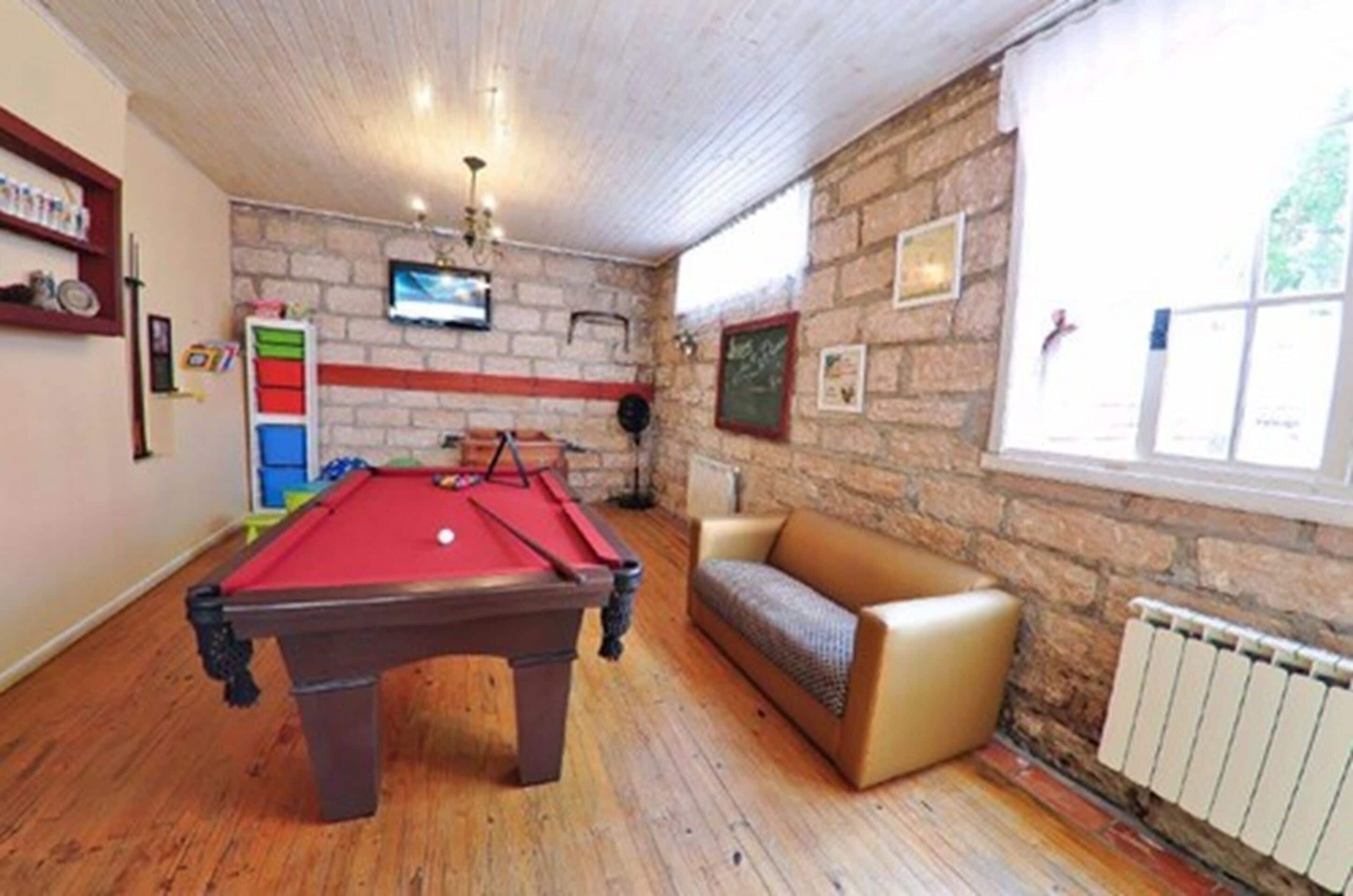 A pool table in a room with a stone wall, a television, and a window.