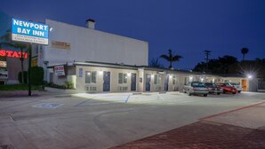 A motel with a sign for Newport Bay Inn, a parking lot with handicap-accessible spaces, and several cars parked in front. - Newport Bay Inn (Costa Mesa)